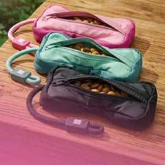 Drei Max & Molly Training Food Dummys  in Pink, Mint und Grau, geöffnet und mit Leckerlis gefüllt, auf Holztisch.